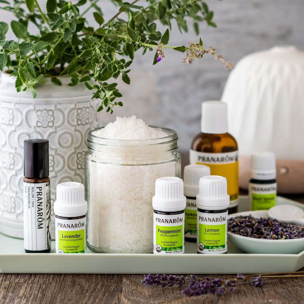Pranarom Certified Organic Roller, Lavender Essential Oil, Peppermint Essential Oil, Frankincense Essential Oil, Lemon Essential Oil bottles with salt jar and plants.