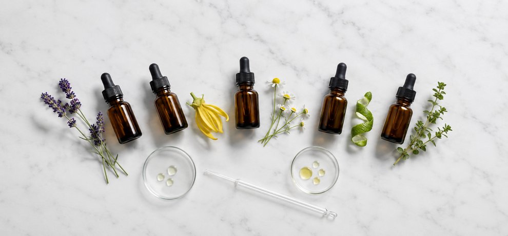 Five amber Essential Oil bottles with lavender, ylang ylang, chamomile, bergamot and marjoram on a white surface