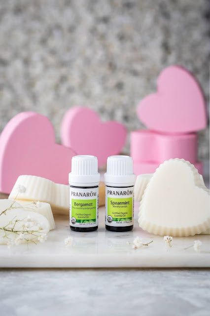 Pranarom Certified Organic Bergamot and Spearmint Essential Oil bottles with hand soaps and pink hearts in the background.