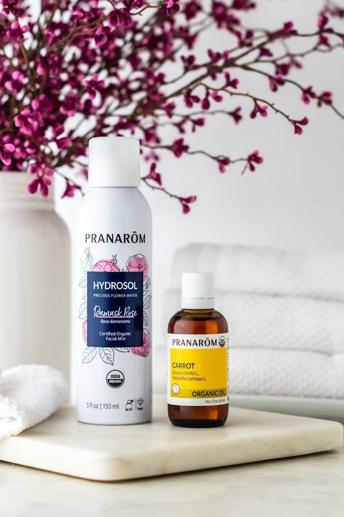 Pranarom Certified Organic Damask Rose Hydrosol Facial Mist and Carrot Virgin Plant Oil with towels and flowers.